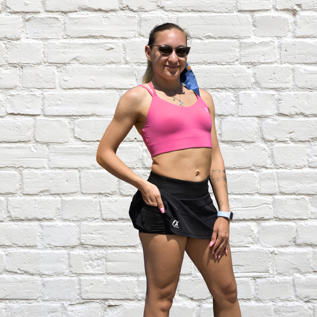 female model wearing pink sports bra and black tennis skirt showing its pocket features