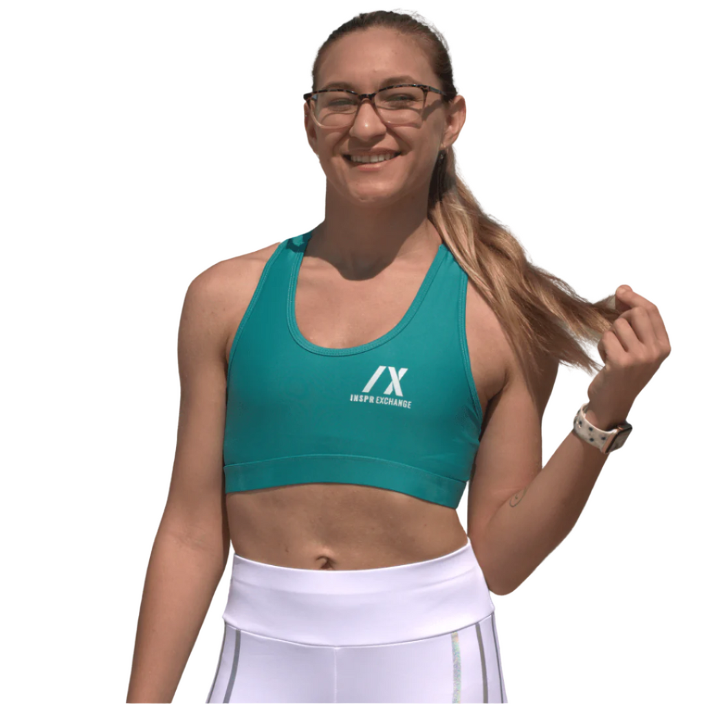 female athletic model posing for inspr exchange athletica while wearing teal green virago sport bra with white leggings
