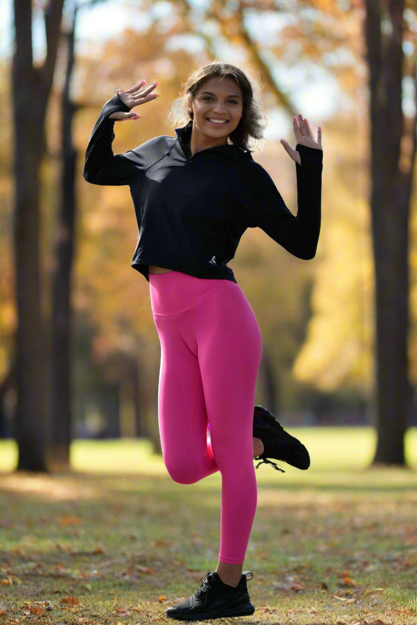 female model posing for inspr exchange athletics on a gorgeous day while wearing black fleece pullover and pink leggings while standing on one feet